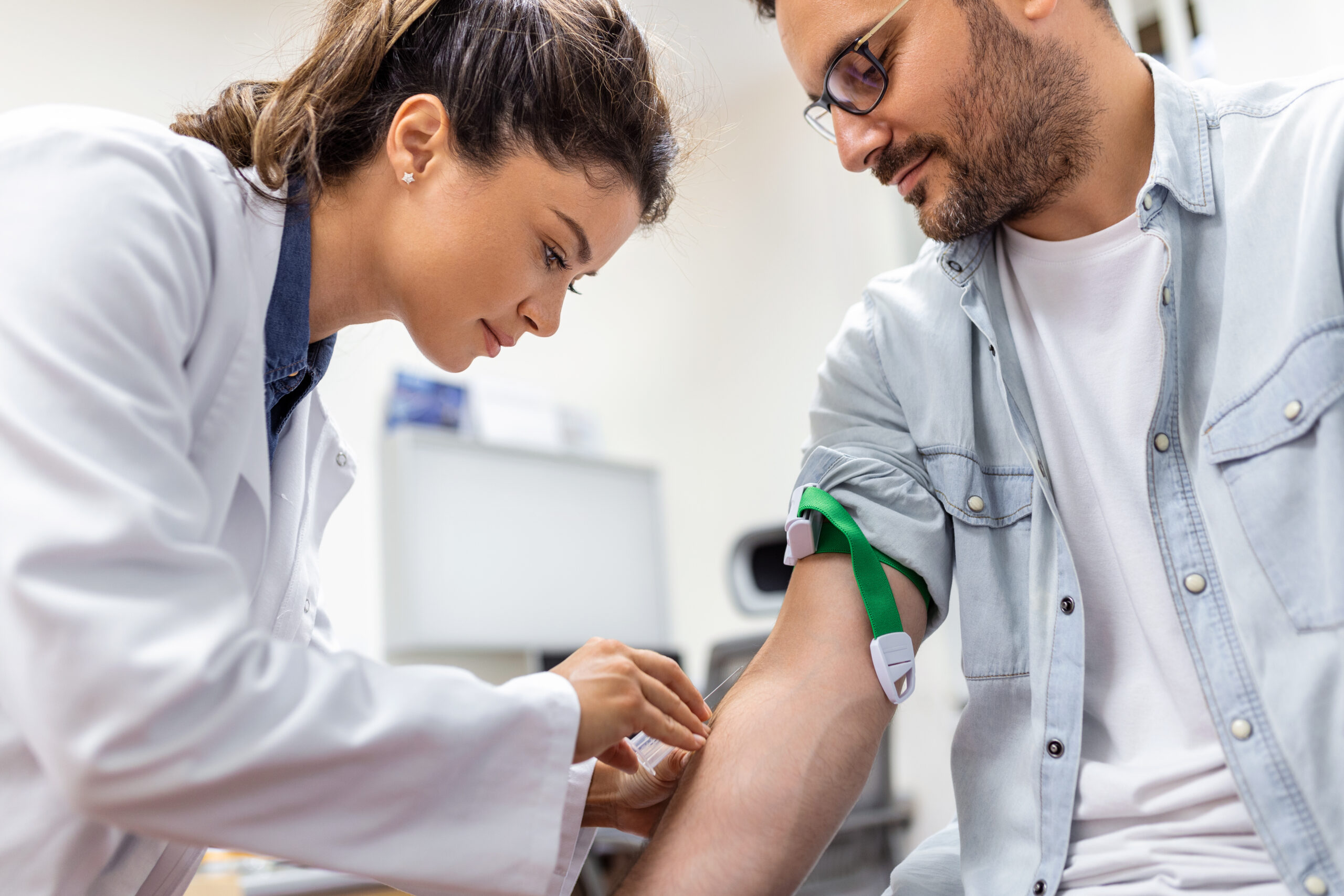 Friendly hospital phlebotomist collecting blood sample from patient in lab. Preparation for blood test by female doctor medical uniform on the table in white bright room