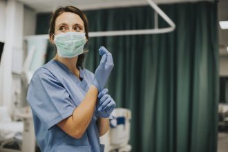 Female nurse with a mask putting on gloves